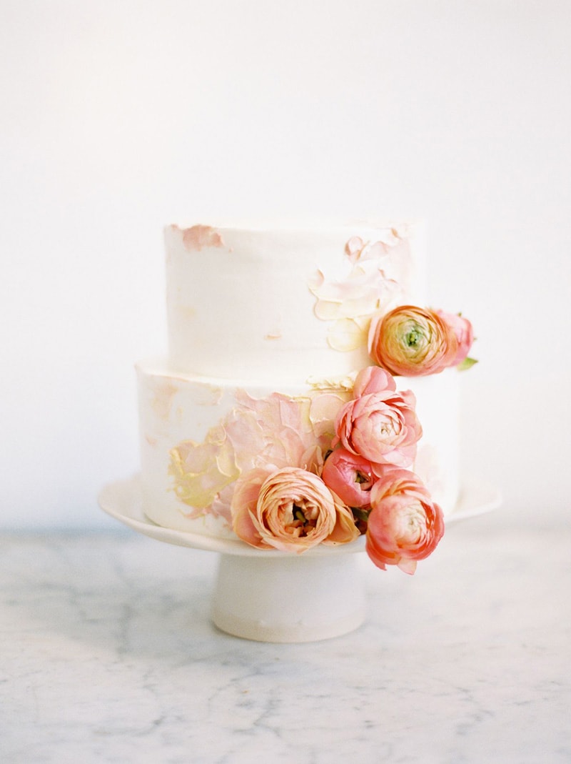 Romantic Boho Desert Pastel Wedding Ideas | An elegant two tier buttercream wedding cake decorated with palette knife painted detail in pale blush and yellow tones and cascading salmon pink and peach ranunculus. | Photography: Ciara Richardson via Once Wed