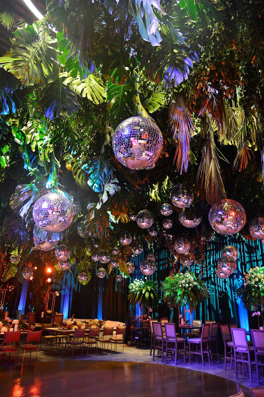 Electric Disco Wedding Ideas |  Modern greenery installation at a wedding reception suspended above the dance floor featuring tropical leaves, palm fronds and dozens of mirror balls of all different sizes | Photography: Ana Hinojosa & Sergio Sandona via Brides