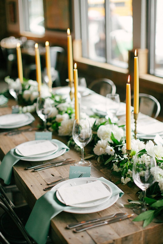 Rustic reception centrepiece with mustard yellow candlesticks and green and white floral table runner | Laura Ivanova via Style Me Pretty