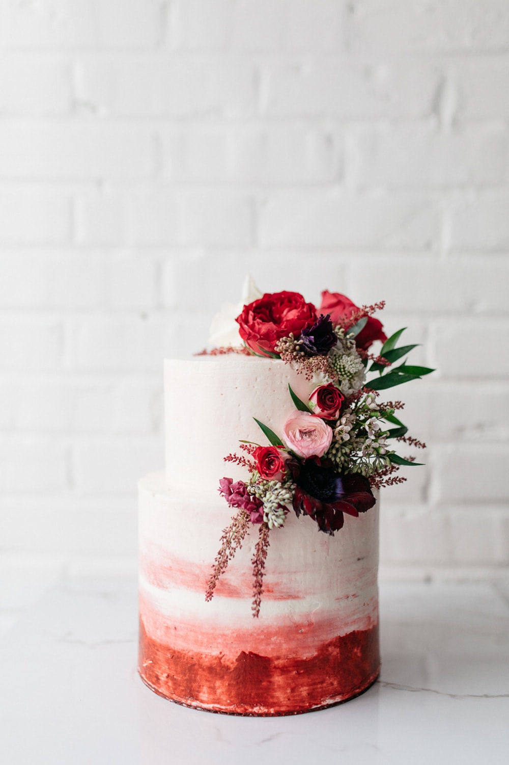Modern Red & Pink Wedding Ideas | A rustic two tier white buttercream wedding cake with a cascade of red, pink and white flowers on the top tier and red and pink watercolour detail on the bottom tier. | Photography: Carrie Mcguire via Green Wedding Shoes