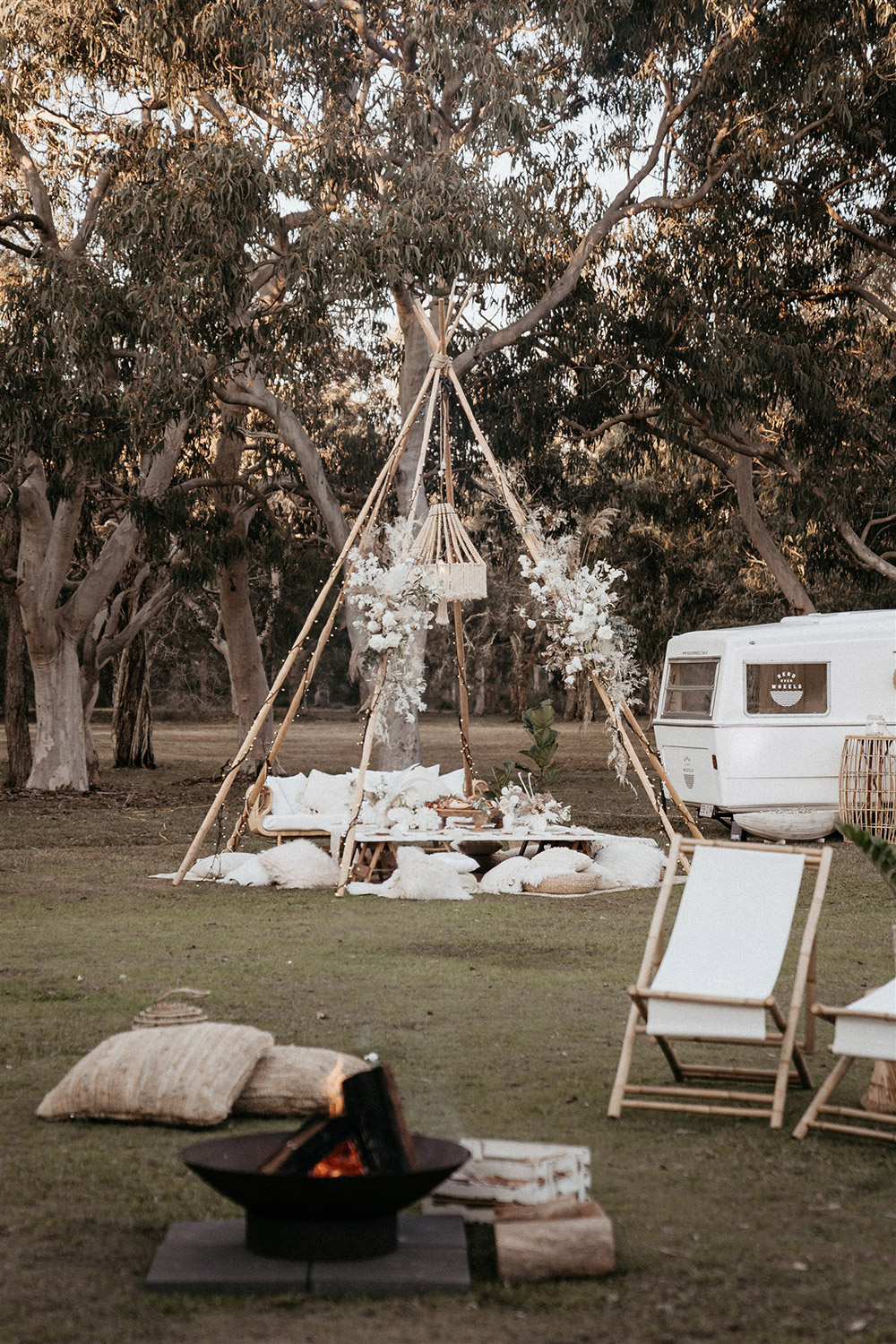 Outdoor Festival Bohemian Wedding Inspiration | A naked tipi wrapped in fairy lights and sprays of boho florals is set for picnic style grazing. Beneath a beaded and fringed chandelier sits layered rugs, scattered cushions in neutral and white textures and a low table set for eight. This is topped with a macrame runner and clusters of white vessels displaying fresh posies. | Photography: Shae Estella Photo