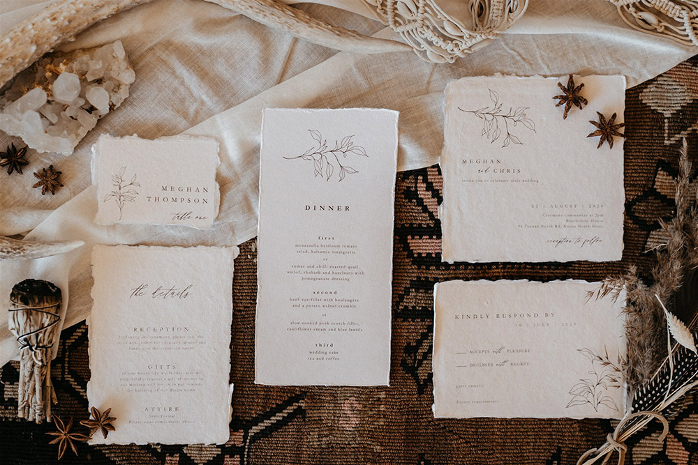Outdoor Festival Bohemian Wedding Inspiration | A boho wedding stationery suite on white deckle edge cotton paper features a fine line foliage motif and modern vintage serif font paired with flowing script. The suite consists of a wedding invitation, a card providing "The Details" on the reception, gifts and attire, a "Kindly Respond By" RSVP card, an escort card with the guest name and table number, and a dinner menu. | Photography: Shae Estella Photo