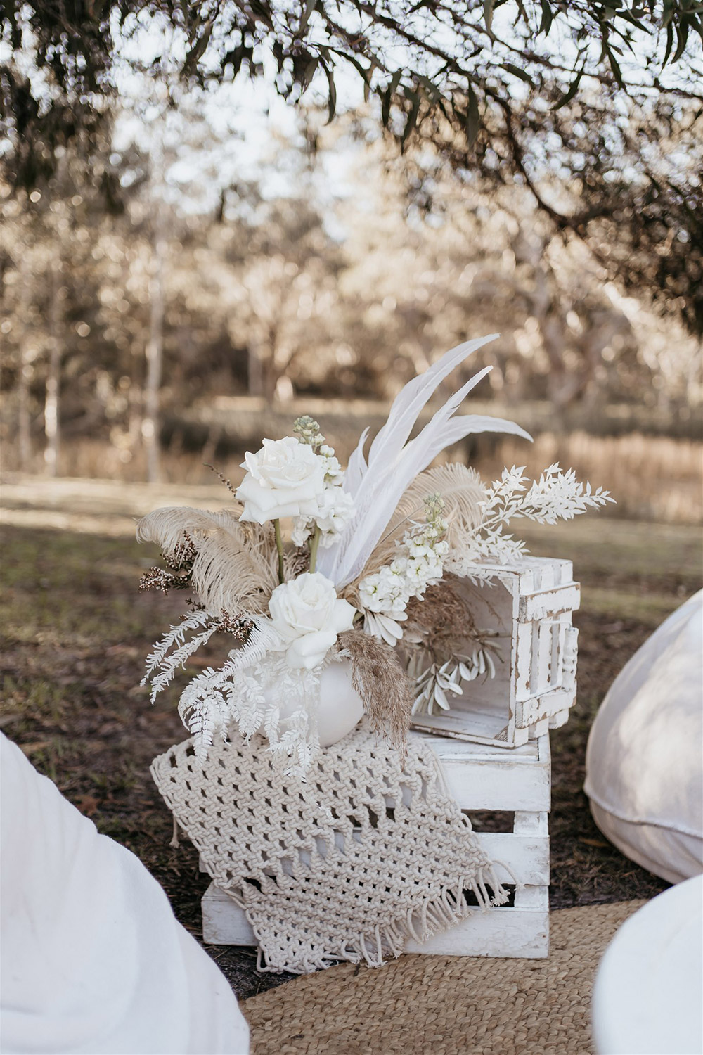 Outdoor Festival Bohemian Wedding Inspiration | Rustic white stacked crates are decorated with a macrame runner and small vase of white and neutral flowers, feathers and foliage for a boho outdoor cocktail style wedding reception. | Photography: Shae Estella Photo