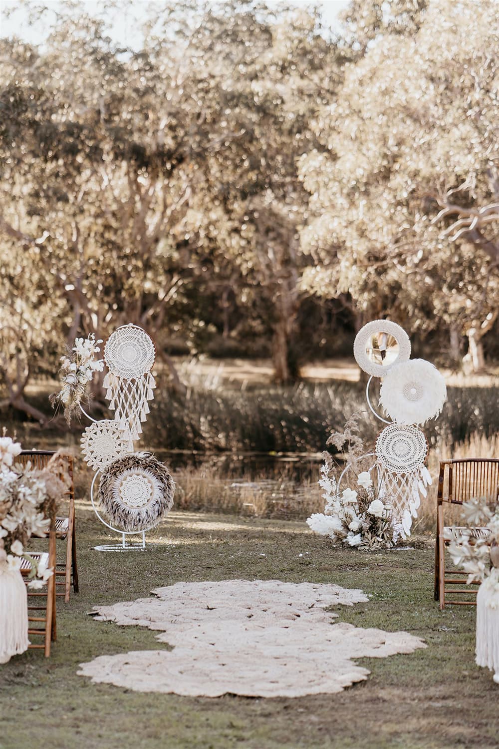 Outdoor Festival Bohemian Wedding Inspiration | This outdoor boho wedding ceremony consists of woven jute rugs for the aisle and two pillars of white circles in varying sizes adorned with macrame, feathers and flowers for the arbour. The setting is framed by bamboo folding chairs for guests and large white vases decorated with fringed macrame wraps that are filled with neutral dried floral arrangements accented with stems of white tulips, stocks, cotton and ruscus. | Photography: Shae Estella Photo