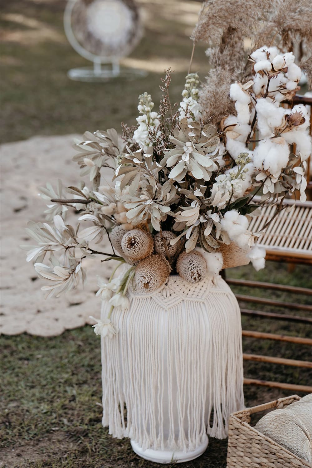 Outdoor Festival Bohemian Wedding Inspiration | This outdoor boho wedding ceremony consists of woven jute rugs for the aisle and two pillars of white circles in varying sizes adorned with macrame, feathers and flowers for the arbour. The setting is framed by bamboo folding chairs for guests and large white vases decorated with fringed macrame wraps that are filled with neutral dried floral arrangements accented with stems of white tulips, stocks, cotton and ruscus. | Photography: Shae Estella Photo