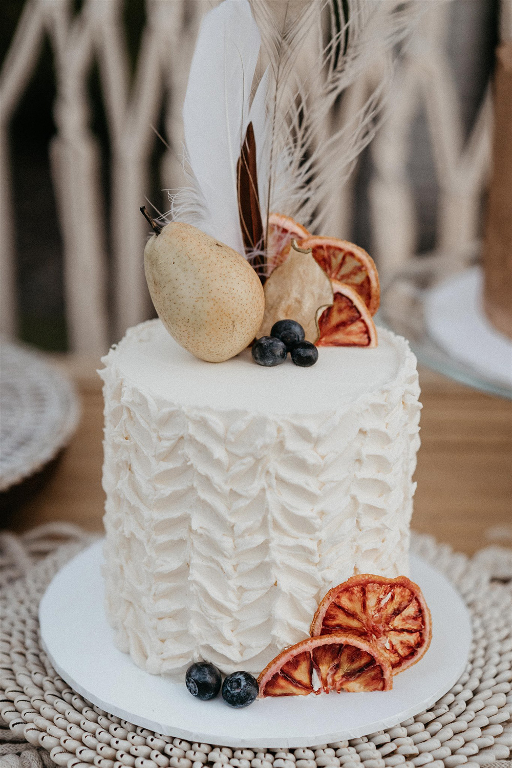 Outdoor Festival Bohemian Wedding Inspiration | A second single tier white buttercream wedding cake features bold chevron texture, dried orange slices, whole pear, blueberries and assorted feathers. | Photography: Shae Estella Photo