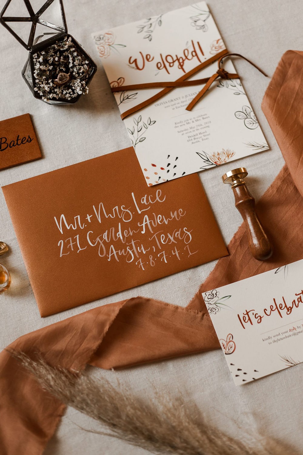 Boho Rust & White Wedding Ideas | An illustrated wedding stationery suite incorporating natural motifs in earthy tones on cream coloured card and tied with leather cord reads, "We eloped! Let's celebrate." The accompanying envelope is rust coloured with the address handwritten in modern white calligraphy. | Photography: Wild Love Photography via Intimate Weddings 