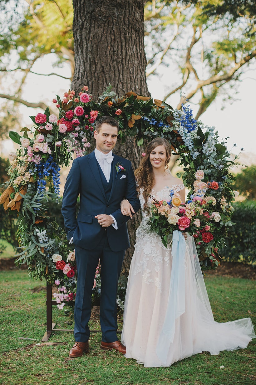 Whimsical garden wedding ceremony with circular arbour featuring bright multicolour flowers | Lover of Mine
