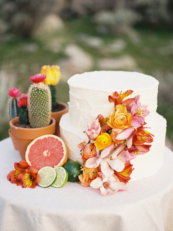 Tropical wedding cake topped with bright coral, pink and yellow flowers styled with potted cacti and citrus fruits | Chelsea Scanlan via Ruffled